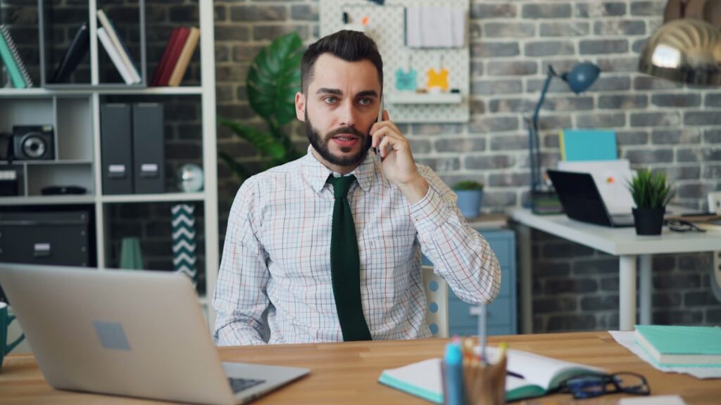 Small business owner on phone with an MCA relief specialist, looking relieved at their desk