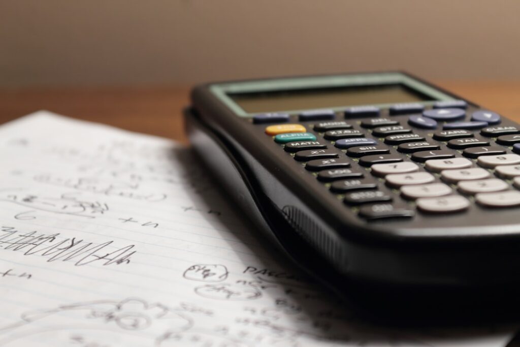 Calculator showing MCA factor rate calculations next to stacked loan documents