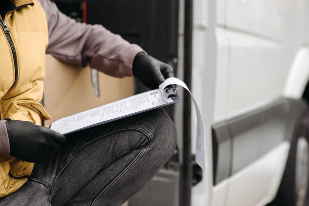 Courier contractor checking route paperwork beside a delivery van
