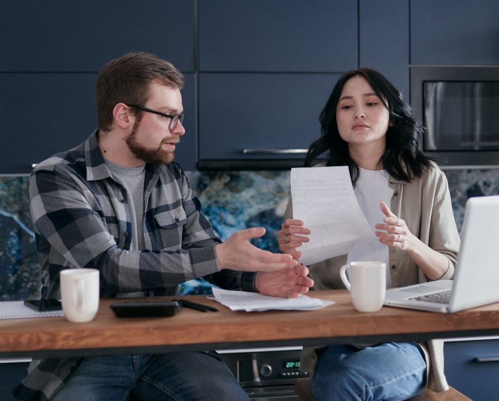 Small business owner reviewing overdue bills and a laptop at a kitchen table