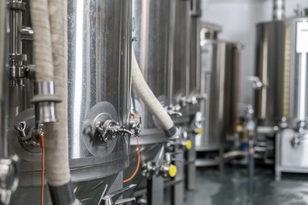 Stainless steel brewery fermentation tanks with a paperwork clipboard nearby