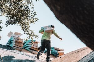 Roofing contractor reviewing an insurance claim document while standing on a ladder against a house
