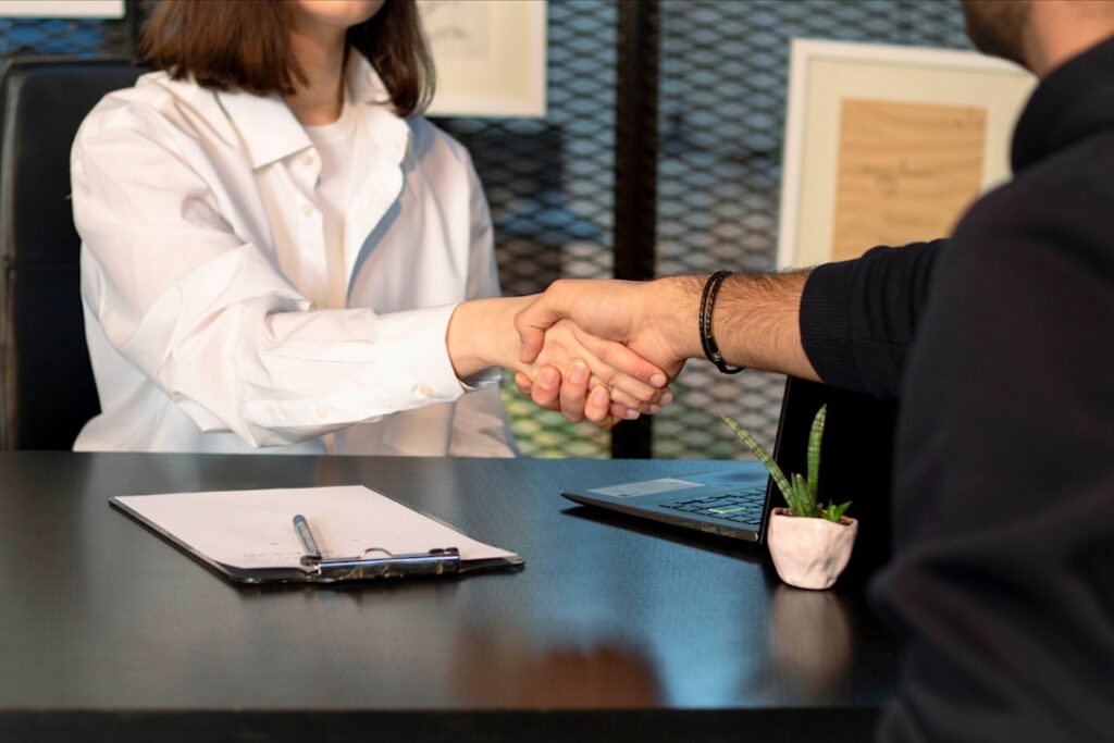 Two people shaking hands across a desk after a negotiated settlement