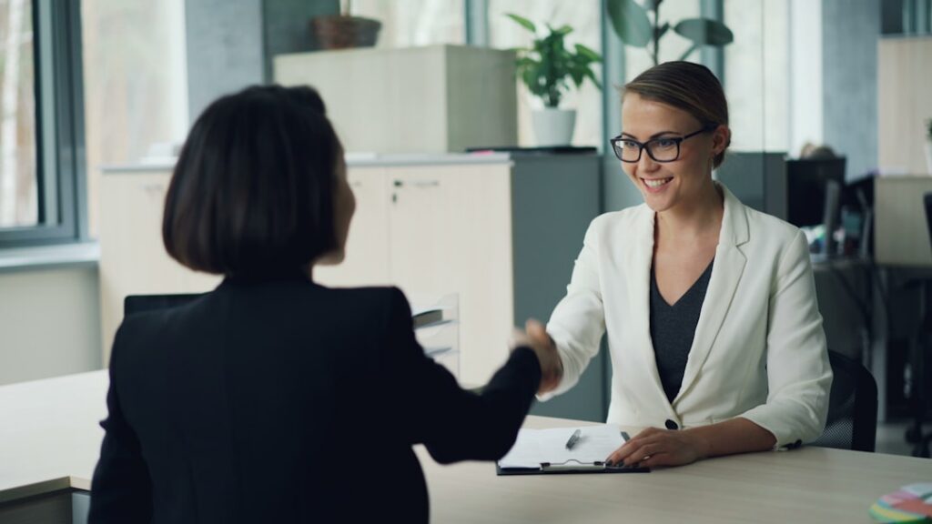 Two business professionals shaking hands across a desk during a negotiation