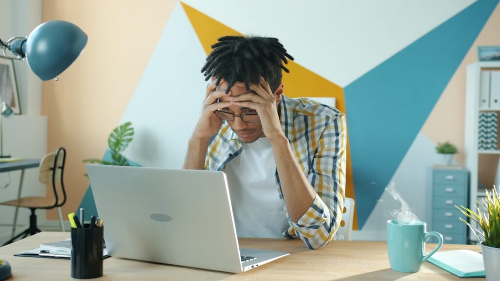 Small business owner looking stressed at laptop reviewing financial documents early in the morning