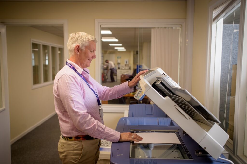 Print shop owner reviewing invoices beside a wide-format printer during a busy production run
