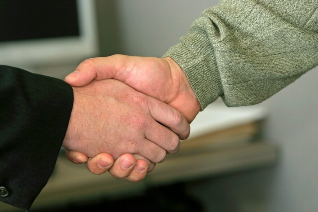 Two people shaking hands across a desk after signing an agreement