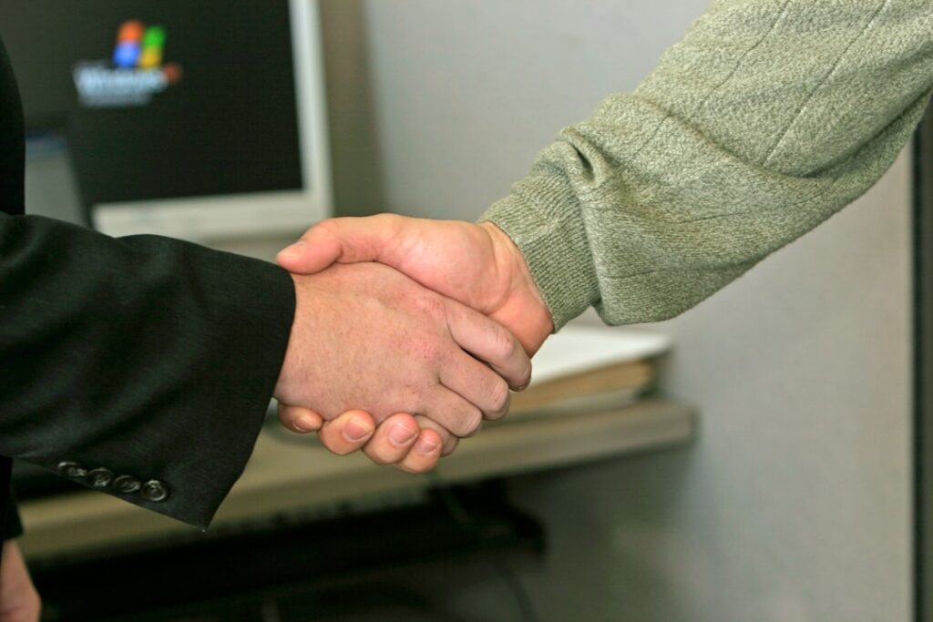 Two people shaking hands across a small office desk after reaching an agreement