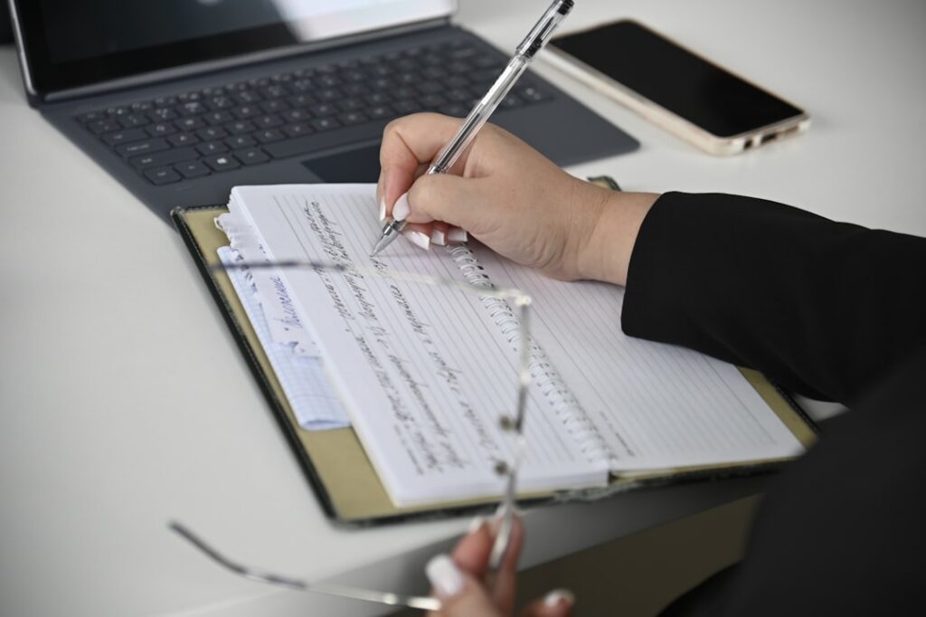Business owner writing a check while reviewing a bank statement on a laptop