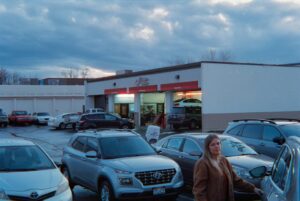 Rows of used cars on a dealership lot with a small sales office
