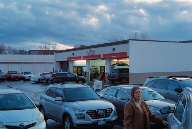 Rows of used cars on a dealership lot with a small sales office