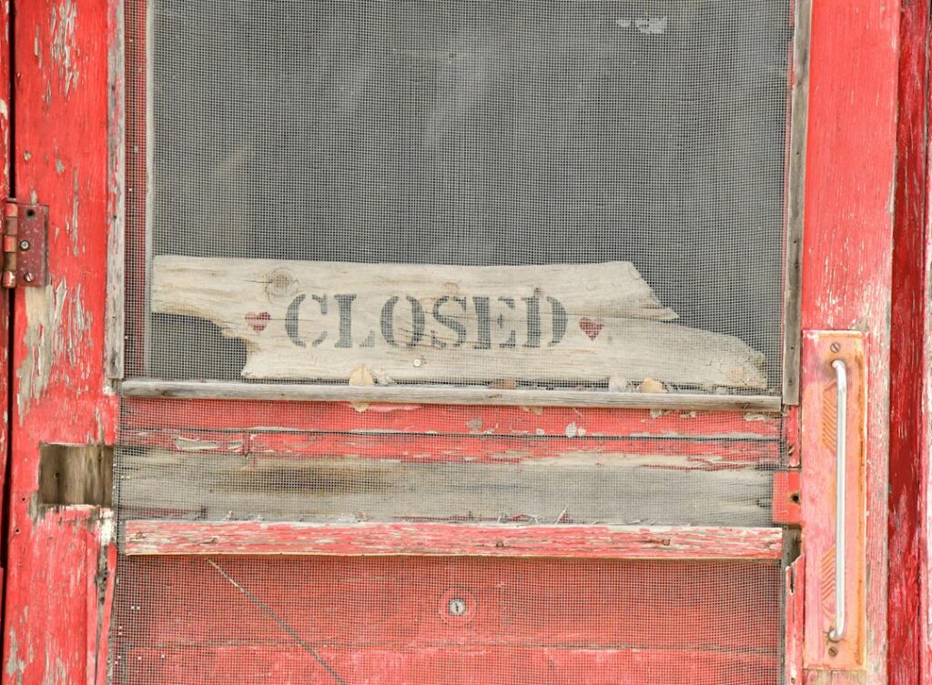 Closed small business storefront with storm damage, owner reviewing paperwork outside